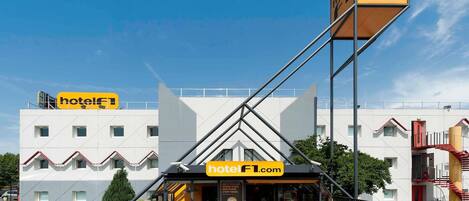 A hotel with a modern design, featuring a prominent entrance, outdoor seating area, and a clear sky.