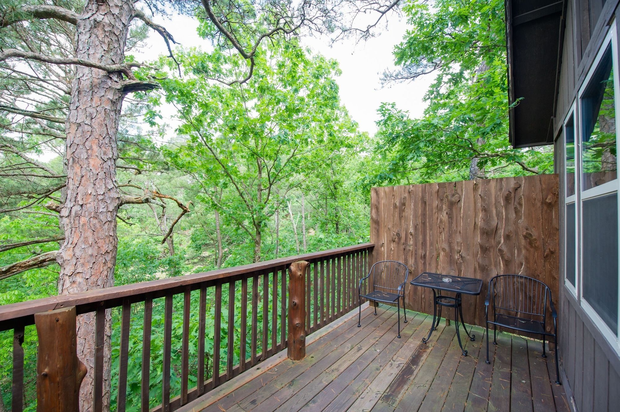 A wooden deck with a railing, two metal chairs, and a table.