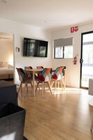Un comedor moderno con una mesa y sillas de madera, un televisor de pantalla plana montado en la pared y un gran ventanal corredizo que da a un espacio exterior.