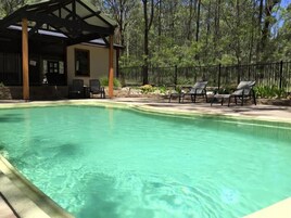 Una piscina con sillones de descanso y un área de estar techada.