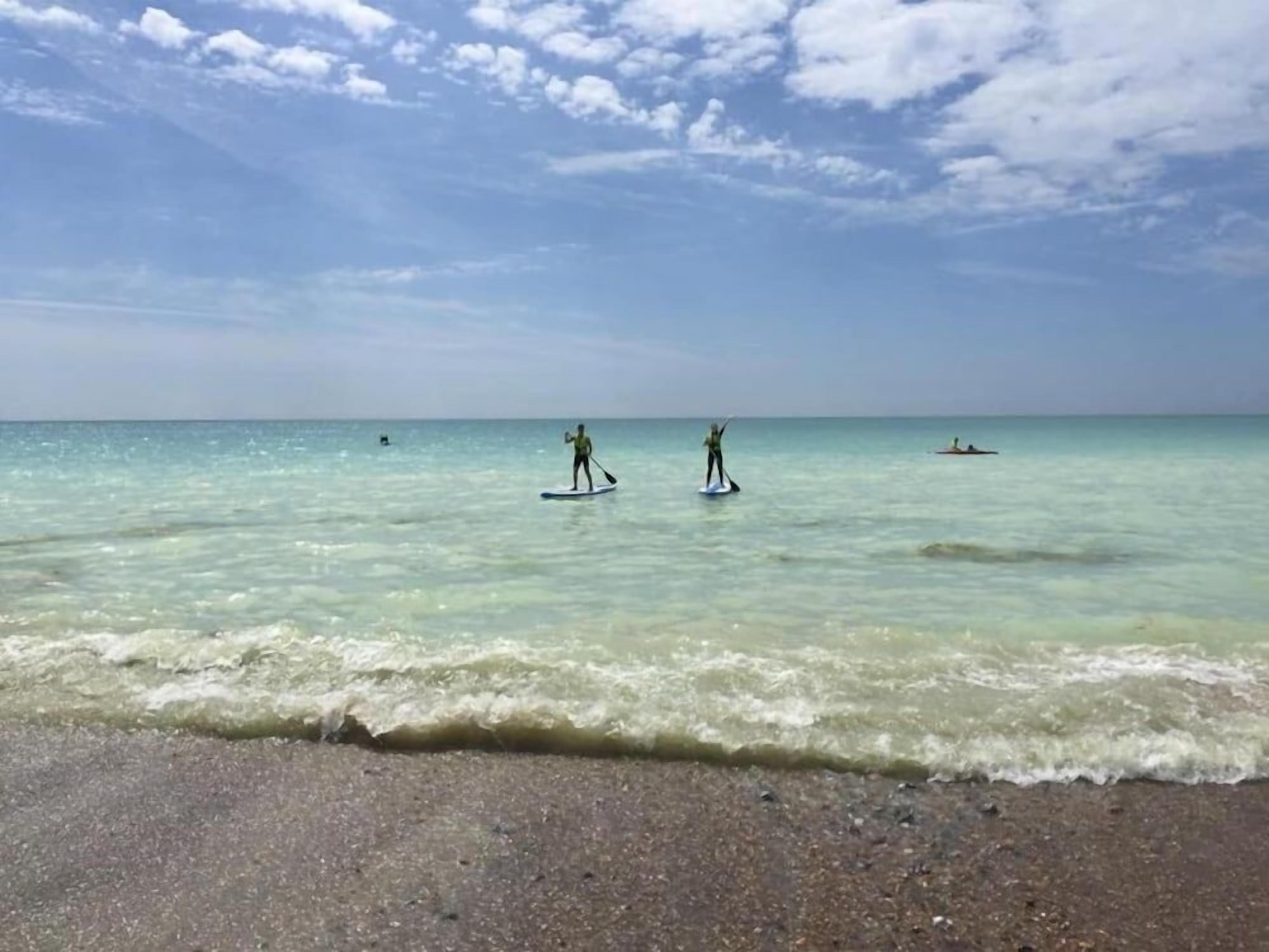 A beach with clear water, a sandy shore, and a few people in the distance.