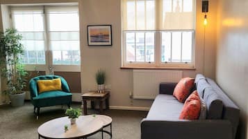 A living room with a sofa, armchair, round coffee table, and a potted plant.