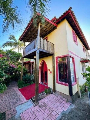 Una casa de dos pisos con balcón, puerta roja y toldo rojo.