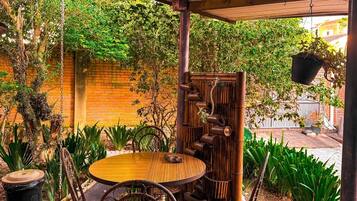 An outdoor patio with a round table and wicker chairs, surrounded by greenery and a bamboo water feature.