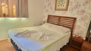 Una cama bien tendida con un cabecero de madera, un estampado floral en la pared y un cuadro enmarcado sobre la cama.