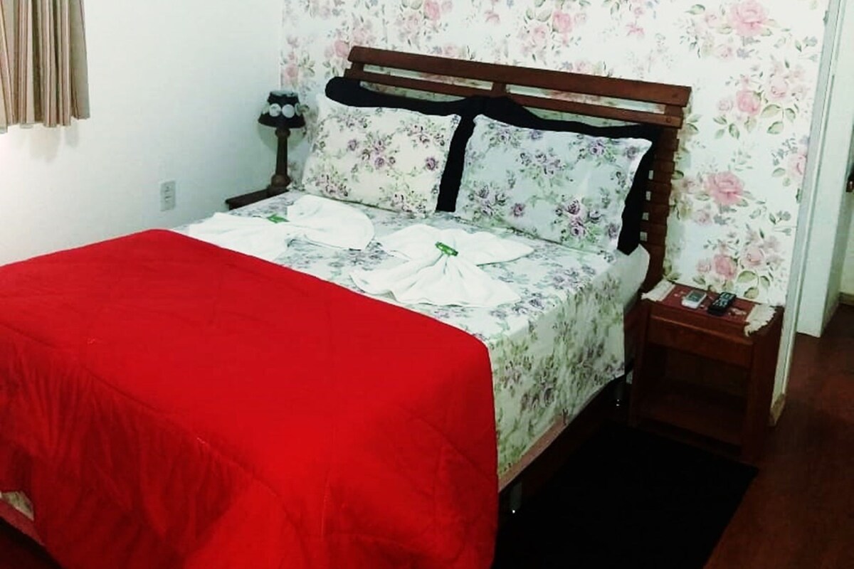 Un dormitorio con cama, mesita de noche, un cuadro enmarcado en la pared y un estampado de papel tapiz floral.