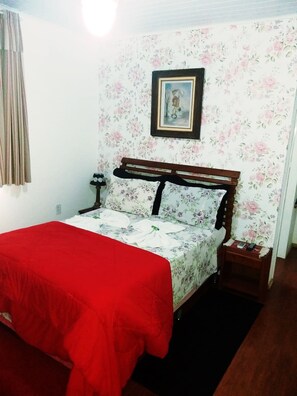 Un dormitorio con cama, mesita de noche, un cuadro enmarcado en la pared y un estampado de papel tapiz floral.