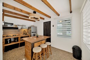 Een kleine keuken met een houten kookeiland, barstoelen, een magnetron en een koelkast.