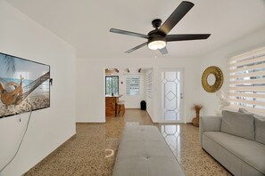 A modern living room with a ceiling fan, a TV, a sofa, and a kitchen area in the background. - Charming 1-bedroom house with AC in peaceful Ciales (Ciales)