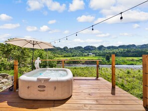 Een hottub op een houten terras met uitzicht op een rivier en begroeiing.