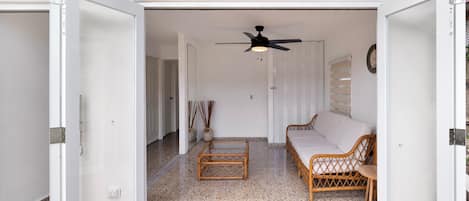 An open doorway leading to a living room with a ceiling fan, a sofa, a coffee table, and a wicker chair.