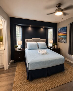 A bedroom with a bed, nightstands, a ceiling fan, and a painting on the wall. - Shark Tooth Acres Manasota Key Retreat 4/3.5 (Englewood)