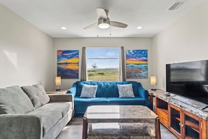 A living room with a blue sofa, grey couch, TV, and artwork on the walls. - Manasota Key | 4BR 3.5BA | Sleep 14 (Englewood)