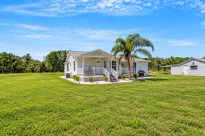 A single-story house with a porch, a small front yard, and a palm tree. - Shark Tooth Acres Manasota Key Retreat 4/3.5 (Englewood)