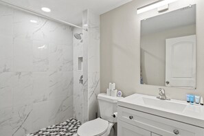 A bathroom with a shower, toilet, sink, and mirror. - Shark Tooth Acres Manasota Key Retreat 4/3.5 (Englewood)