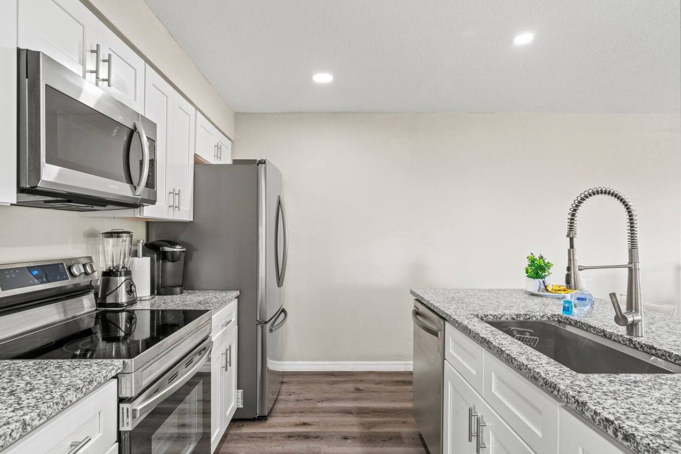 A modern kitchen with stainless steel appliances, granite countertops, and white cabinetry.