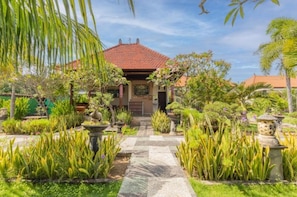 A traditional house with a tiled roof, surrounded by a well-maintained garden with various plants and a stone pathway leading to the entrance. - Townhouse Oak Favorit Bungalows (Bali)