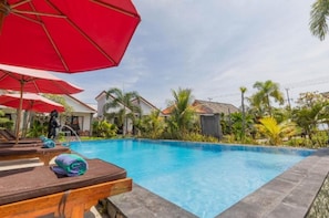 A swimming pool with lounge chairs and umbrellas, surrounded by greenery and buildings. - Townhouse Oak Favorit Bungalows (Bali)