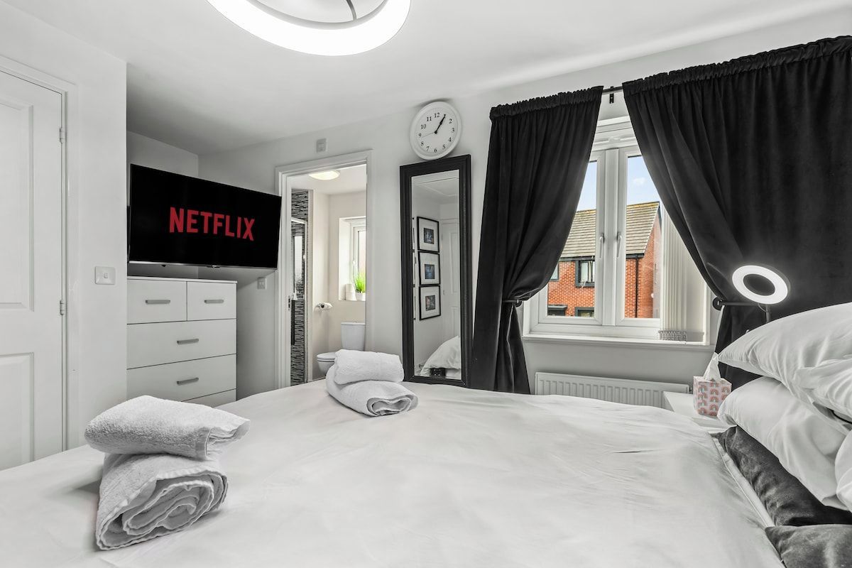Ein Hotelzimmer mit Bett, Fernseher mit Netflix-Logo, einer Uhr und einem Fenster mit Vorhängen.