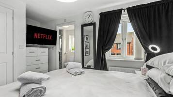 Ein Hotelzimmer mit Bett, Fernseher mit Netflix-Logo, einer Uhr und einem Fenster mit Vorhängen.