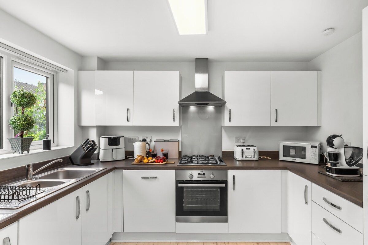 A modern kitchen with white cabinets, stainless steel appliances, and a window with a view of greenery.
