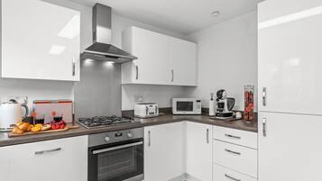 A modern kitchen with white cabinets, a gas stove, a microwave, and a coffee maker.