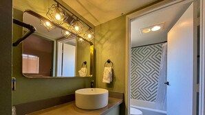Un baño con lavamanos redondo, un espejo con luces, un perchero para toallas y un suelo de ducha estampado.