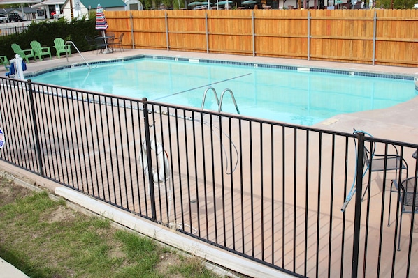 A swimming pool with a metal fence, green chairs, and a wooden fence in the background.