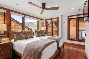 Un dormitorio con dos camas, ventilador de techo y ventanas amplias.
