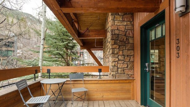 A wooden deck with a stone wall, a green door, and a number '303' on the wall. - Downtown Aspen Collection by Frias (Aspen)