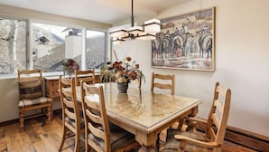 A dining area with a glass-top table, wooden chairs, a vase with dried flowers, and a painting on the wall. - Downtown Aspen Collection by Frias (Aspen)