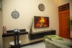 A room with a dartboard, a clock, a fireplace with a fire, a television, and a door.