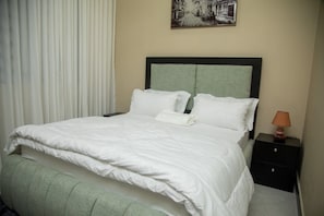 A neatly made bed with white bedding, a headboard, and a nightstand with a lamp.