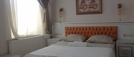 A bedroom with a bed, a nightstand, a wall-mounted air conditioner, a framed floral artwork, and a window with curtains.
