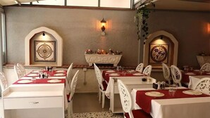 Un restaurante con varias mesas, cada una con mantel rojo y sillas blancas. Hay apliques decorativos en las paredes y una chimenea con un arreglo floral.