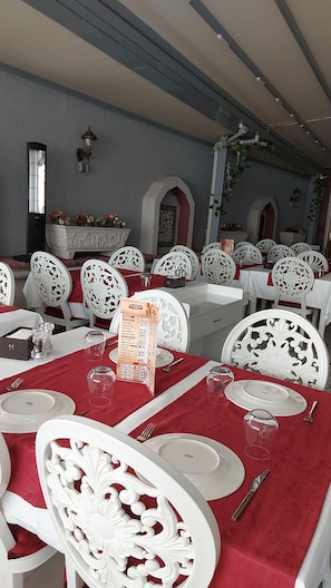 A dining area with white ornate chairs and tables set with red tablecloths.