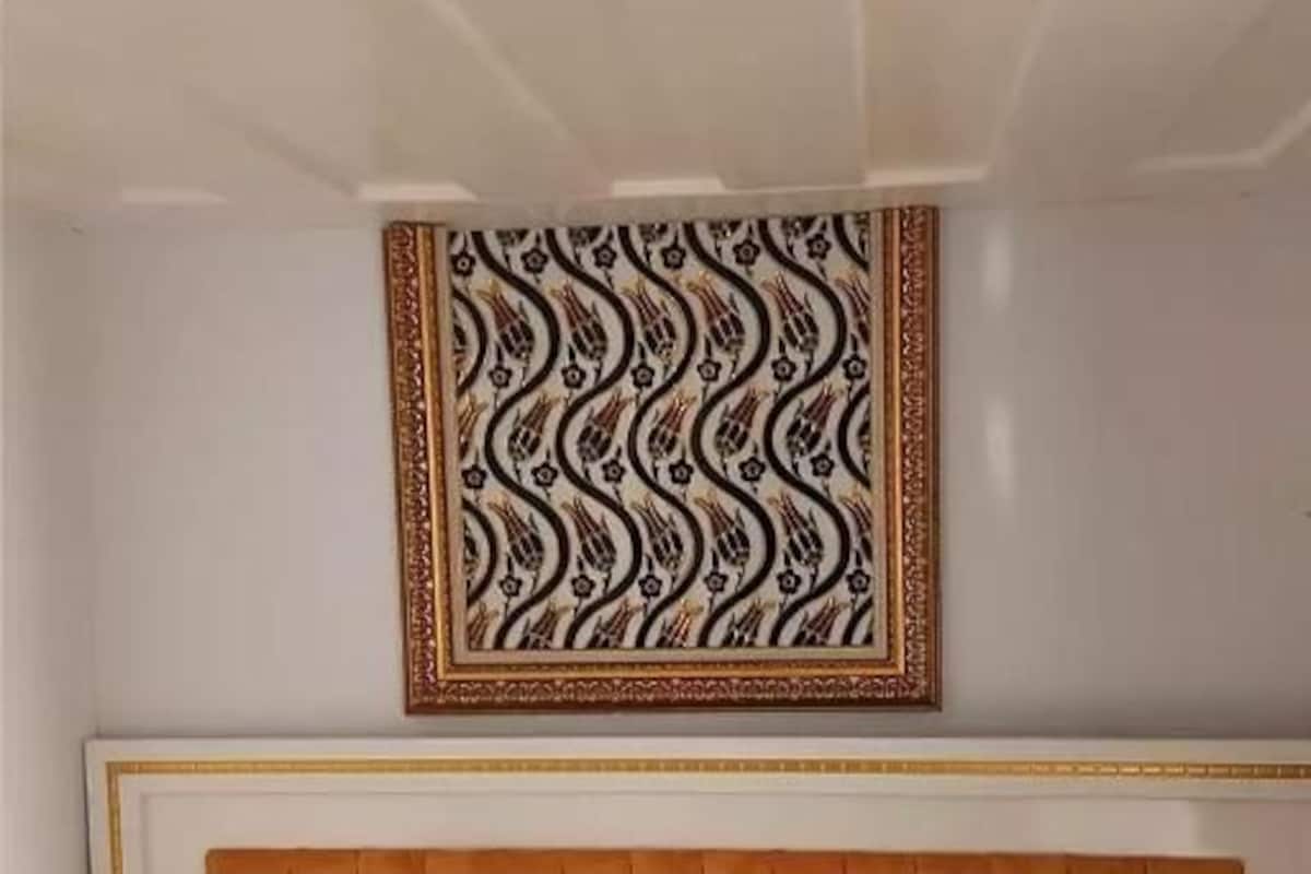 A hotel room with a bed, a headboard, and a patterned wall hanging.