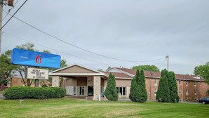 A motel with a sign indicating it is number 6. There is a sign for free WiFi and a phone number. The building has a covered entrance and is surrounded by greenery. - Travel Inn Rockford (Rockford)