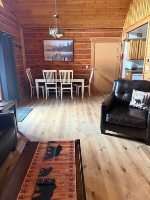 Ein Holzinterieur mit Esstisch, Stühlen, einem schwarzen Ledersofa und einer Fernbedienung auf einem Holztisch.