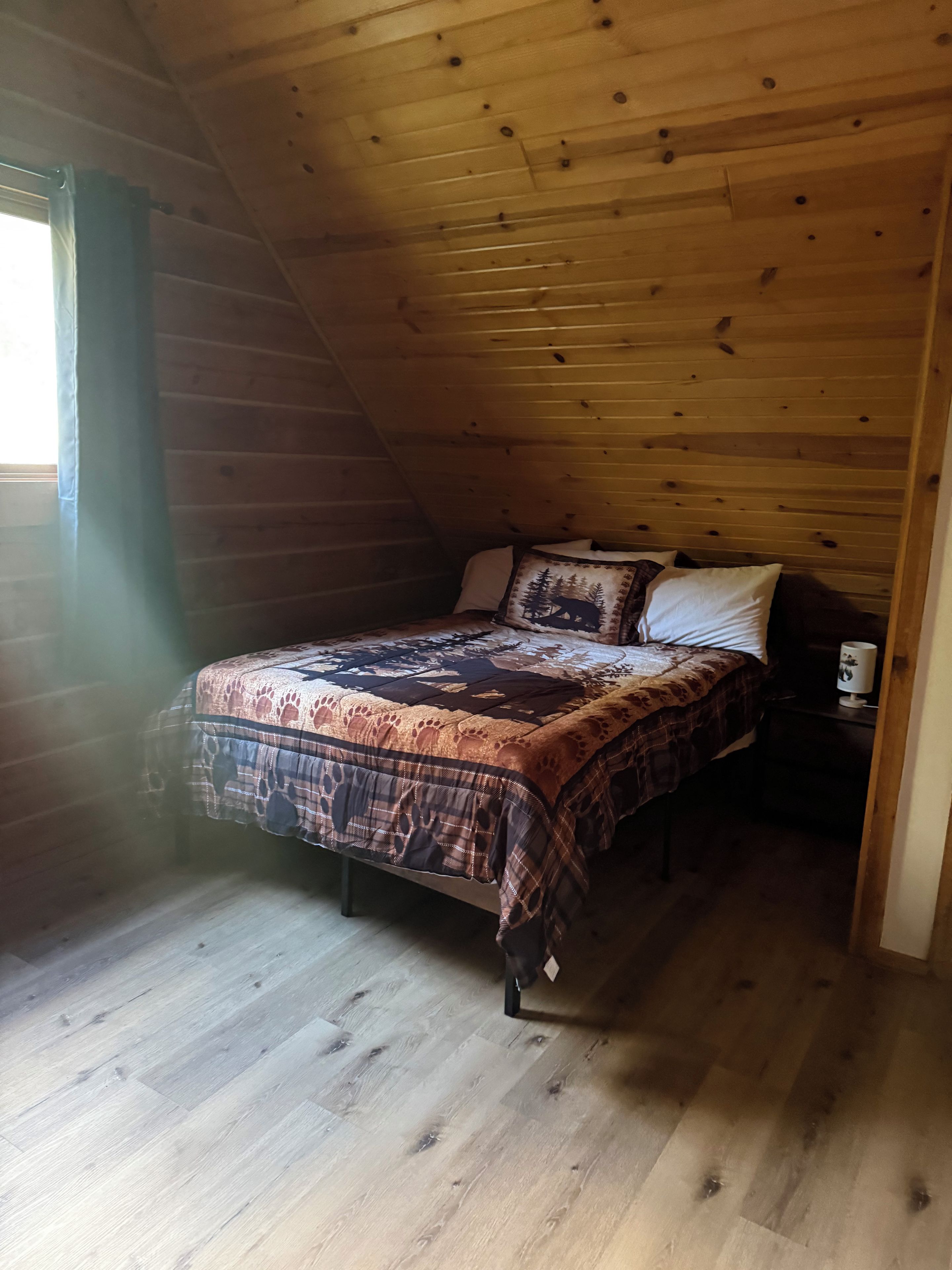 Ein Schlafzimmer mit Holzboden, einem Bett mit gemustertem Überwurf und einem Nachttisch mit Lampe.