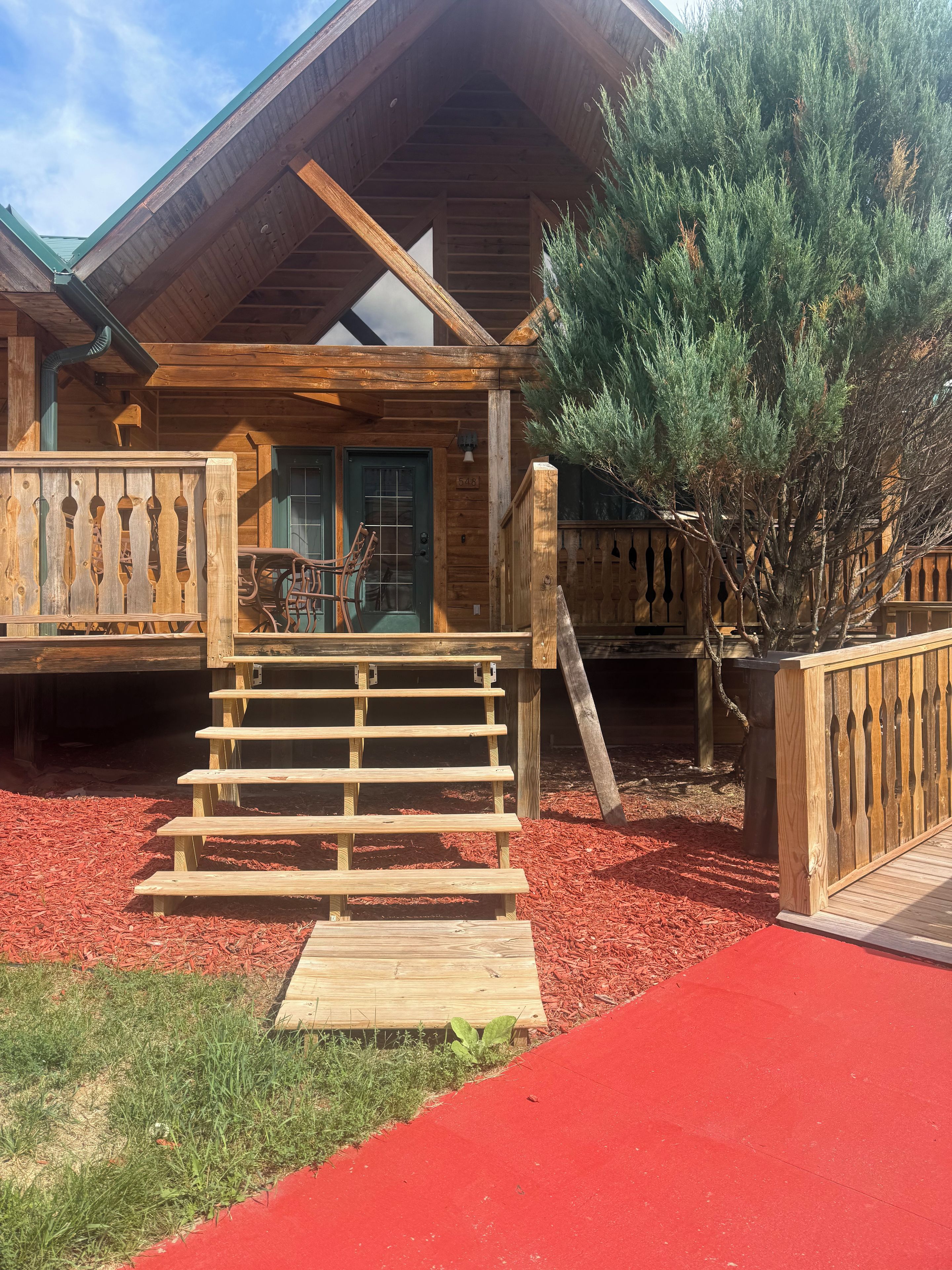Une cabane en bois avec un porche à l’avant, une porte et un petit escalier menant à l’entrée.