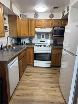 A kitchen with wooden cabinets, a stainless steel sink, a white dishwasher, a stove, and a microwave.