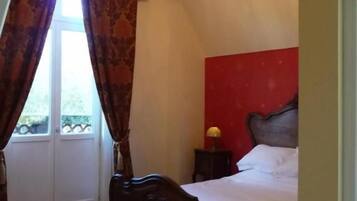 Une chambre à coucher avec un lit, un lustre, une fenêtre avec des rideaux et un mur d’accent rouge.