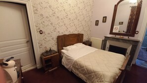 Un dormitorio con una cama, una mesita de noche, un aparador, un radiador y una chimenea.