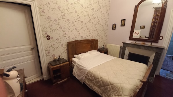 Un dormitorio con una cama, una mesita de noche, un aparador, un radiador y una chimenea.