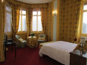 A bedroom with a bed, two chairs, a small table, and a lamp. - Château Lézat  (La Souterraine)