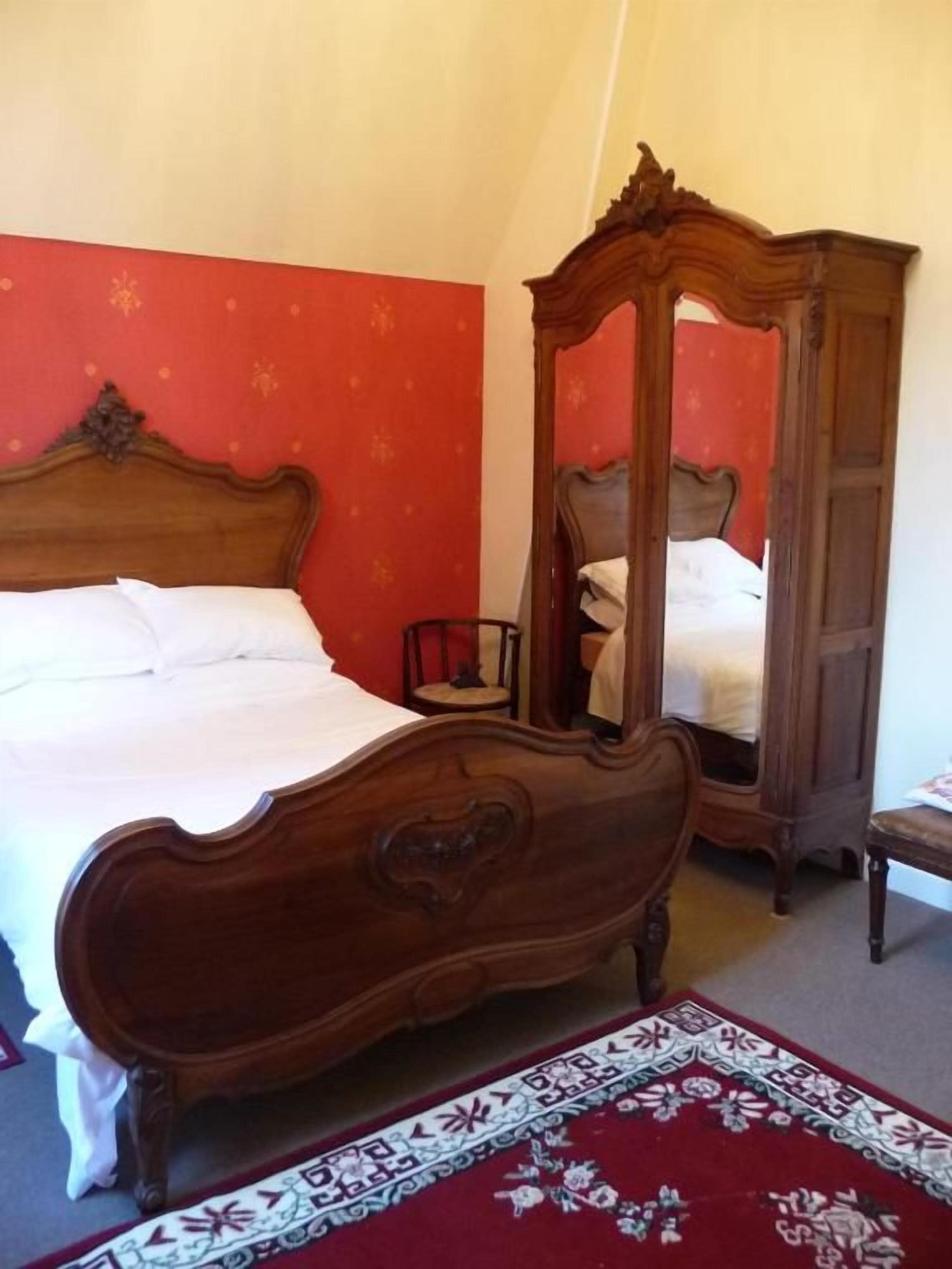 Una camera da letto con un letto di legno, una parete rossa e un mobile contenitore specchiante.