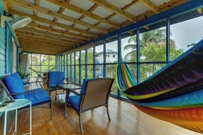 Ein Zimmer mit Holzboden, großen Fenstern, Korbmöbeln und einer Hängematte.