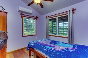 Ein Schlafzimmer mit einem Bett, einem Deckenventilator, einer Klimaanlage und zwei mit Vorhängen versehenen Fenstern.