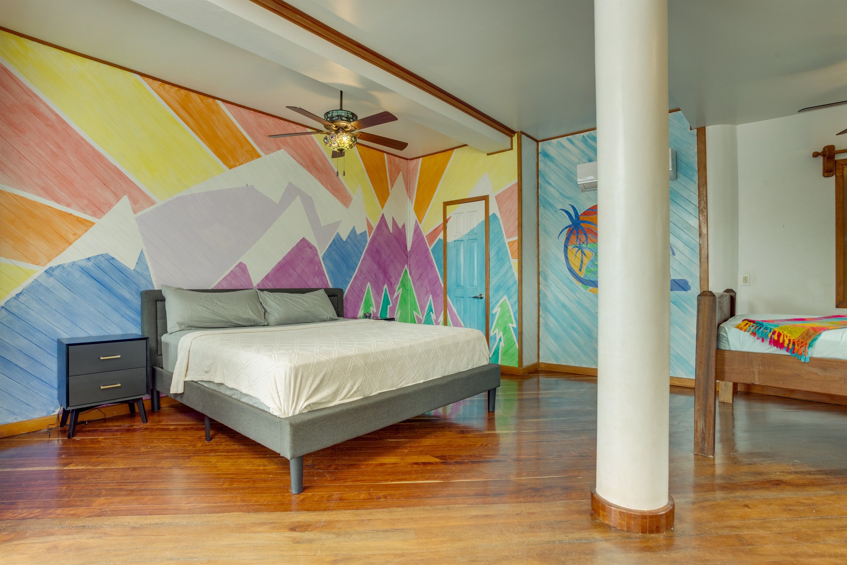 A bedroom with a bed, a nightstand, a ceiling fan, and a colorful wall mural.